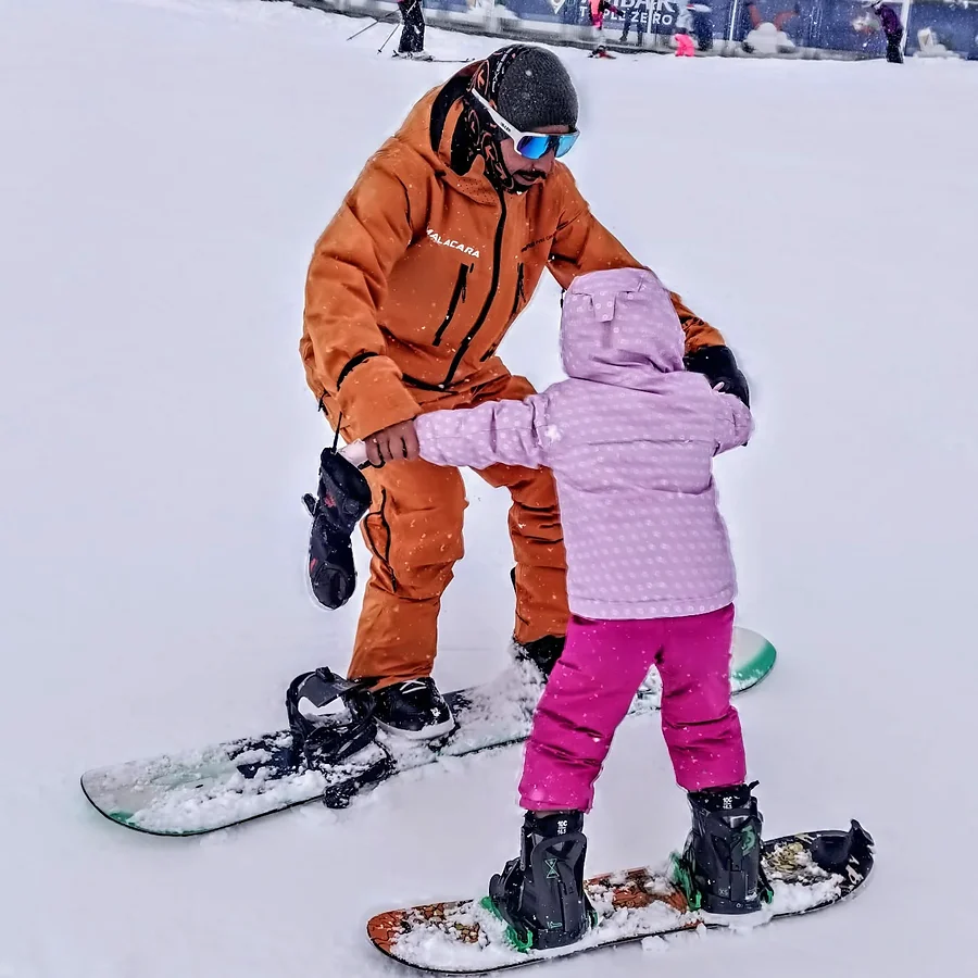 Profesor de Malacara acompañando a una alumna sobre una tabla de snowboard.